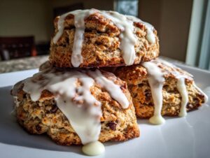 Three freshly baked chocolate chip scones stacked on a white plate, generously drizzled with white glaze.
