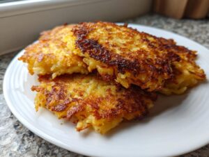 A stack of three perfectly golden brown and crispy potato pancakes served on a white plate.