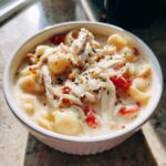 Close-up of a white bowl filled with creamy chicken parmesan soup, featuring shredded chicken, pasta shells, and diced tomatoes.