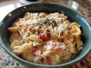 Close-up of a creamy bowl of chicken parmesan soup featuring pasta, tomatoes, and topped with shredded cheese and dried herbs.