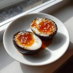 Two halves of dark, marinated eggs with jammy orange yolks, topped with white sesame seeds.