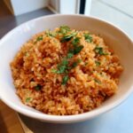 A close-up of a white bowl filled with vibrant orange Mexican rice recipe, topped with fresh cilantro.