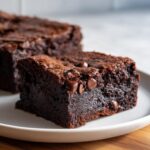 A close-up of a rich, fudgy slice of black bean brownies topped with melted chocolate chips on a white plate.