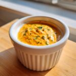 A close-up of thick, orange-hued remoulade sauce speckled with herbs in a small white ramekin.